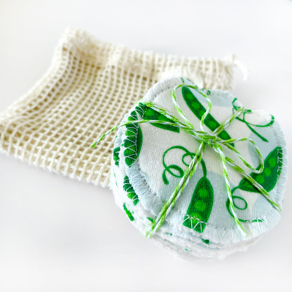 A stack of 10 colorful, green and blue vegetable themed handmade organic cotton reusable facial rounds by Sunny Day Designs is shown stacked and tied with green baker's twine with an eco-friendly wash bag.
