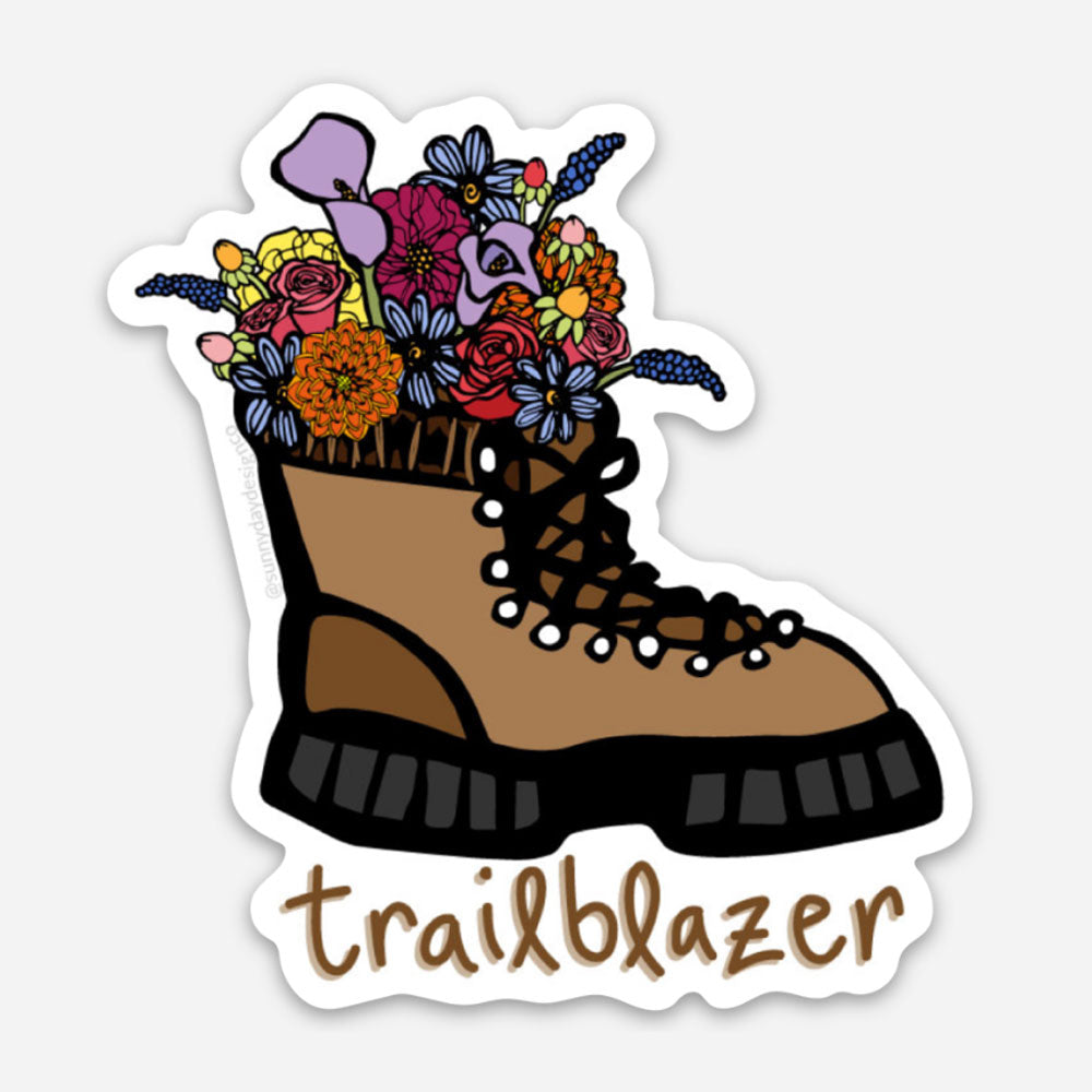A cute hiking boot-themed vinyl sticker by Sunny Day Designs features a brown hiking boot filled with colorful wildflowers with handwritten "Trailblazer" text below.