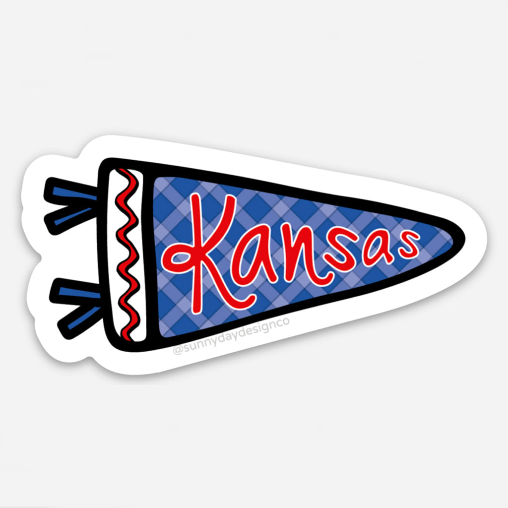 Vinyl sticker in the shape of a pennant flag with a blue and navy checkered background and the word “Kansas” in bold red script. Decorated with black and red tassels and die-cut with a white border, designed by Sunny Day Designs to celebrate Jayhawk pride.