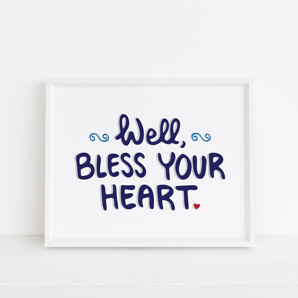 Framed 8x10 art print by Sunny Day Designs featuring the phrase 'Well, Bless Your Heart' in navy blue with a small red heart accent and decorative swirls, displayed on a white background.