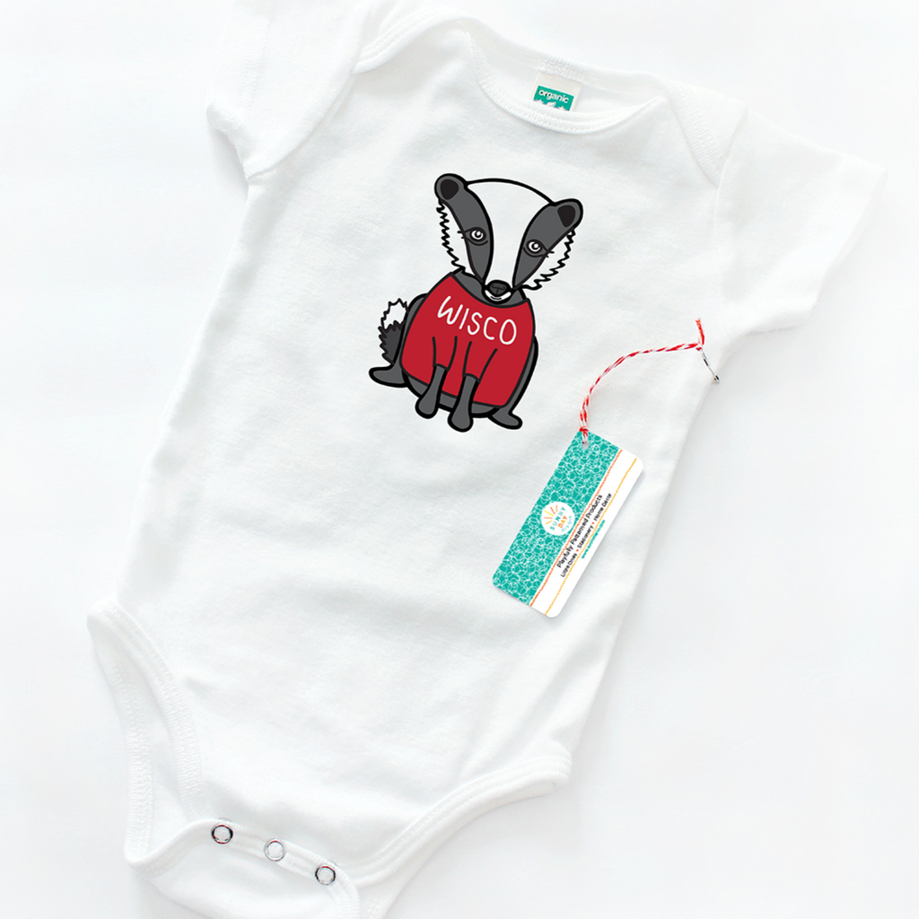 A white organic cotton baby onesie designed for University of Wisconsin Madison fans, with a cute illustration of a gray and white badger wearing a red shirt that says "WISCO" in white lettering. WISCO badger baby onesie design is by Sunny Day Designs and onesie shown on a white background. 