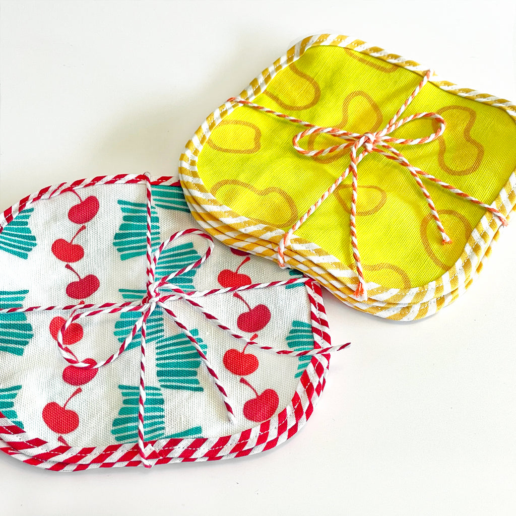 A set of 8 reusable fabric cocktail napkins is shown on a white background and includes 4 red and turquoise stripes cherry-printed fabric cocktail napkins and 4 yellow cheese-printed fabric cocktail napkins.