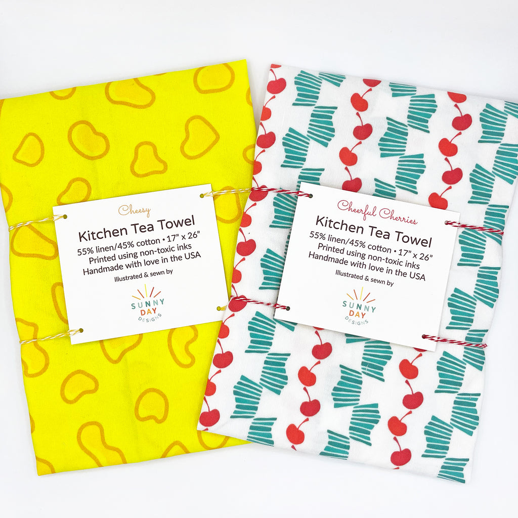 A fun Wisconsin food-themed gift set is shown, which includes 2 WI state-themed tea towels: 1 Yellow and orange cheese-inspired printed linen/cotton dish towel and 1 red, turquoise & white retro-inspired cherry fruit printed tea towel. Both tea towels are handmade in the USA by Sunny Day Designs and feature prints inspired by Wisconsin Cheese and Door County, WI cherries, for which the state of WI is famous!