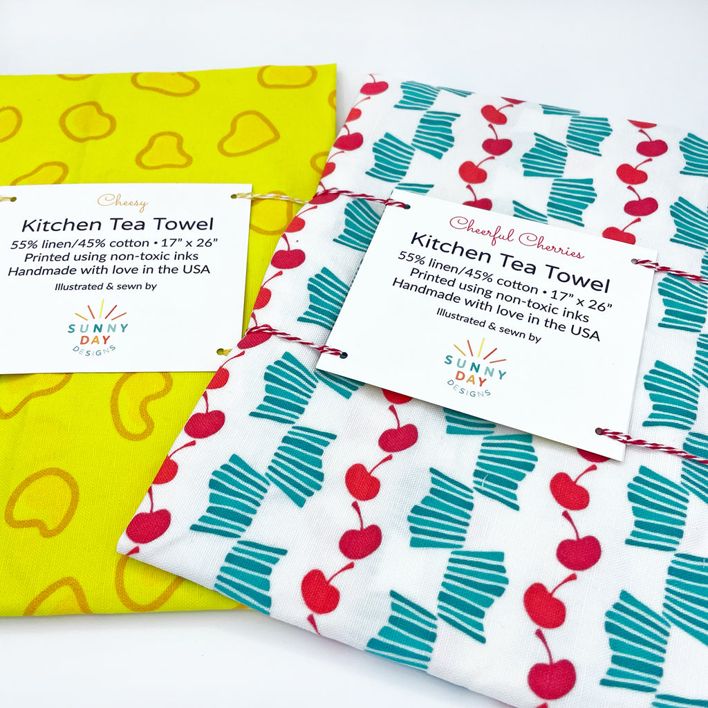 A fun food gift for Wisconsin lovers by Sunny Day Designs is pictured packaged with yellow and red baker's twine against a white background: this set of 2 linen/cotton kitchen towels is handmade in the USA features Wisconsin food prints that will brighten up any kitchen decor! A great Wisconsin travel souvenir or a fun and unique kitchen gift for Wisconsinites.