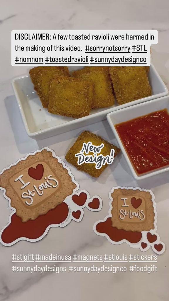 A video showing a plate of toasted ravioli and red marinara dipping sauce (a local food specialty of St. Louis, MO) is shown on a marble countertop alongside a St. Louis-themed toasted ravioli magnet and sticker by Sunny Day Designs. In the video, a hand reaches out to grab a toasted ravioli, dip it in marinara sauce, then a person off-camera takes a bite. Meanwhile, the text "New Design!" appears to highlight that these fun St. Louis souvenir stickers and magnets are a new product recently released.