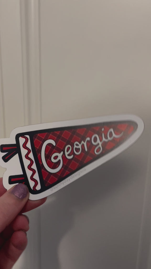 A video showing details of the red, black & white "Georgia Pennant" vinyl magnet by Sunny Day Designs being attached to a metal door. This cute sports magnet would make a great graduation gift, student gift, souvenir of Athens, GA, or a great small gift for any Georgia sports fan! Each of our high quality vinyl magnets is designed in Madison, Wisconsin and made in the USA. 