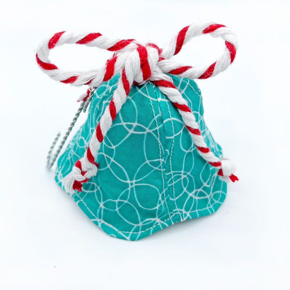 A handmade fabric bell Christmas ornament by Sunny Day Designs feauring a turquoise/white printed fabric with a red/white striped baker's twine bow on top. Made in the USA. Image shown with bell sitting on a white background.