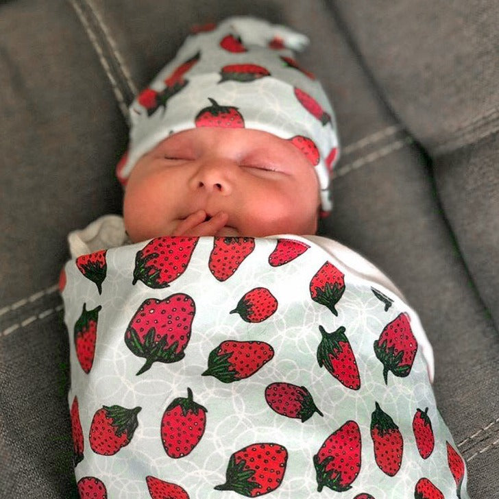bubbly berries organic cotton baby gift set shown on newborn and made in the USA by Sunny Day Designs with newborn hat and baby blanket in red strawberry print design with green stem on gray background