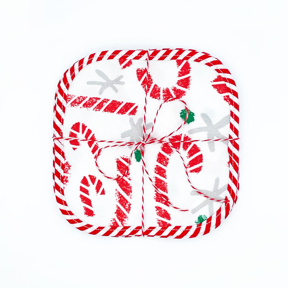A set of 4 packaged Candy Cane Lane Reusable Fabric Cocktail Napkins by Sunny Day Designs. Made in the USA of linen/cotton fabric with red/white striped binding around each square. Packaged with baker's twine on a white background.