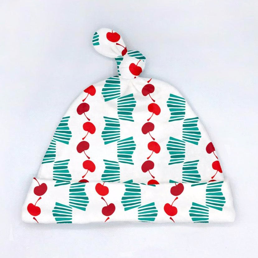 An adorable, cherry-printed  organic cotton baby hat featuring turquoise, Red, and white  and a cute tied-top design