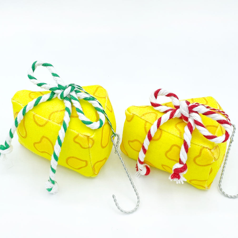 2 cheese Christmas ornaments made by Sunny Day Designs out of organic cotton fabric are shown sitting on a white background. The yellow cheese slice ornaments are handmade from organic cotton fabric in Madison, Wisconsin. 1 ornament features a green/white striped bow and the other ornament features a red/white bow.