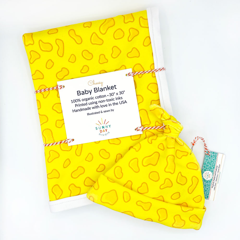 cheesy organic cotton baby gift set made in the USA by Sunny Day Designs with newborn hat and baby blanket in yellow cheese print design with orange holes on yellow background