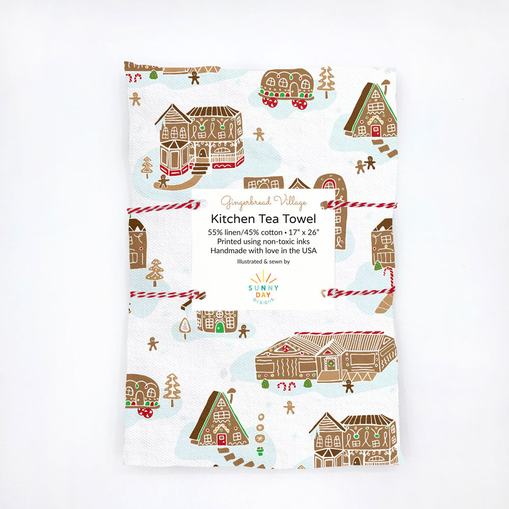 Gingerbread Village holiday tea towel by Sunny Day Designs. This printed linen/cotton Christmas tea towel is packaged and folded on a white background. Made in the USA.
