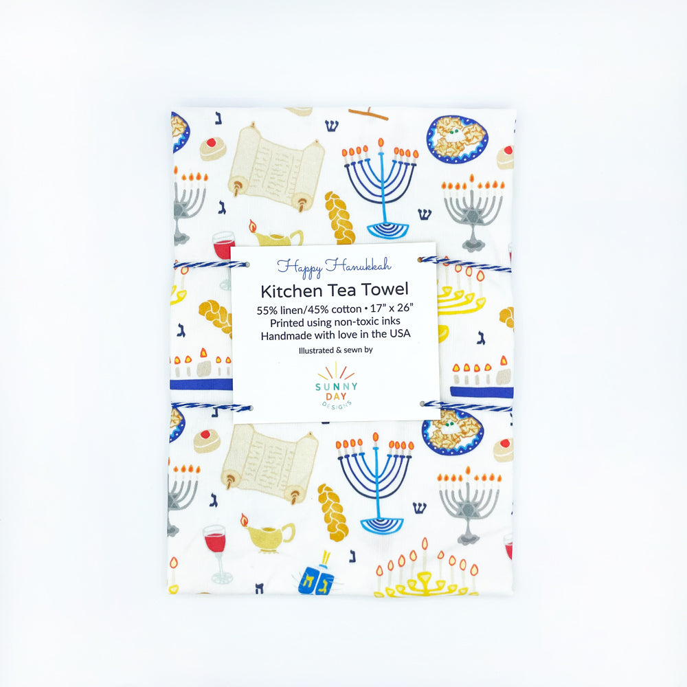 You'll love this colorful Happy Hanukkah printed kitchen dish towel by Sunny Day Designs is packaged using blue baker's twine and folded on a white background. Each fun dish towel is made in the USA & features illustrated menorahs, dreidels, latkes, challah & more Chanukah favorites!