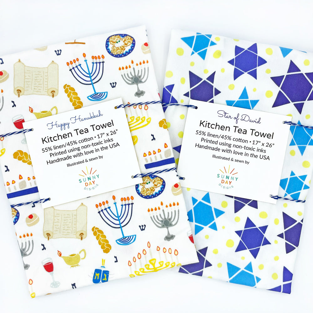 You'll love this set of 2 handmade Jewish tea towels by Sunny Day Designs, which feature our illustrated Happy Hanukkah printed dish towel and our Star of David kitchen towel design. Packaged with blue baker's twine and shown side by side on a white background. Joyfully made in the USA.