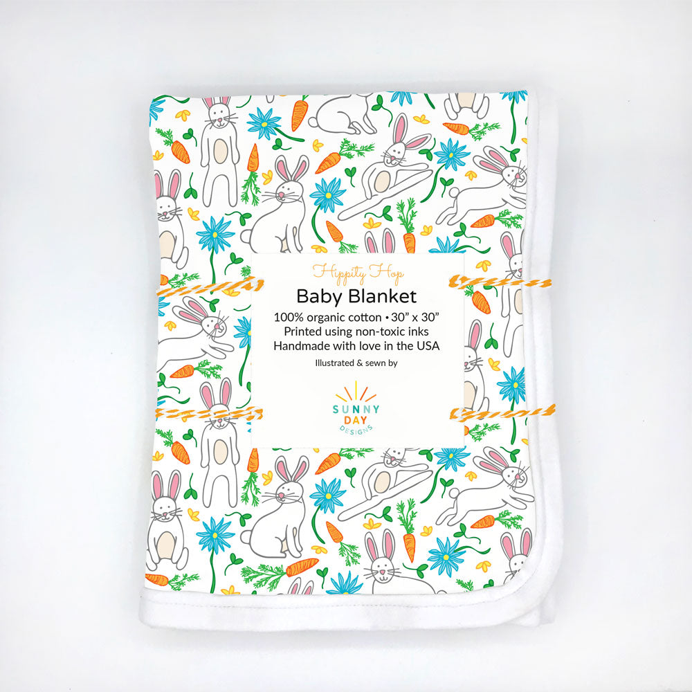 A folded and packaged "Hippity Hop" bunny rabbit printed organic cotton baby blanket by Sunny Day Designs is shown on a white background. Made in the USA and perfect for Sping babies or for baby's first Easter!