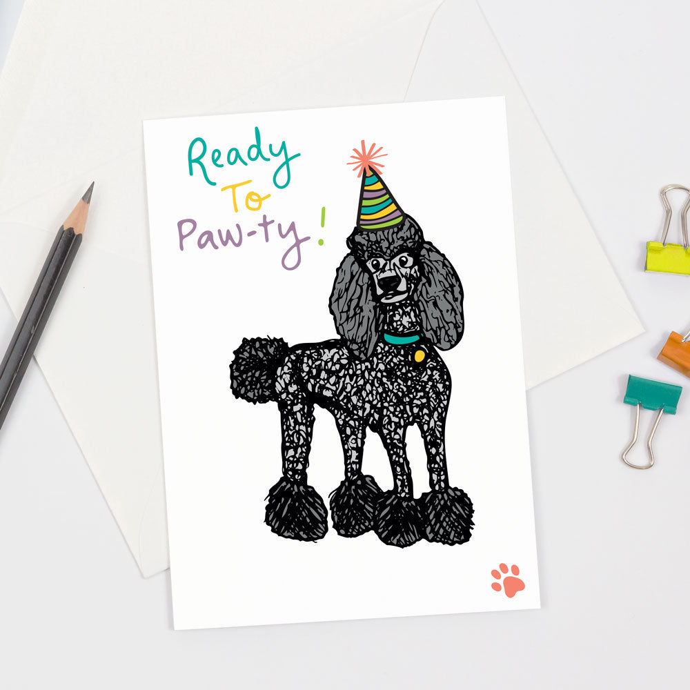 Birthday party greeting card featuring a black poodle dog wearing a colorful party hat, pink paw print, and the words "Ready To Paw-ty" on the front. Designed by Sunny Day Designs and made in the USA.