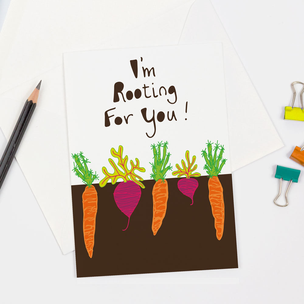 A cute & sustainably sourced root vegetable-themed greeting card by Sunny Day Designs features a cover with carrots & radishes growing below the soil with hand lettered text saying "I'm Rooting For You!"