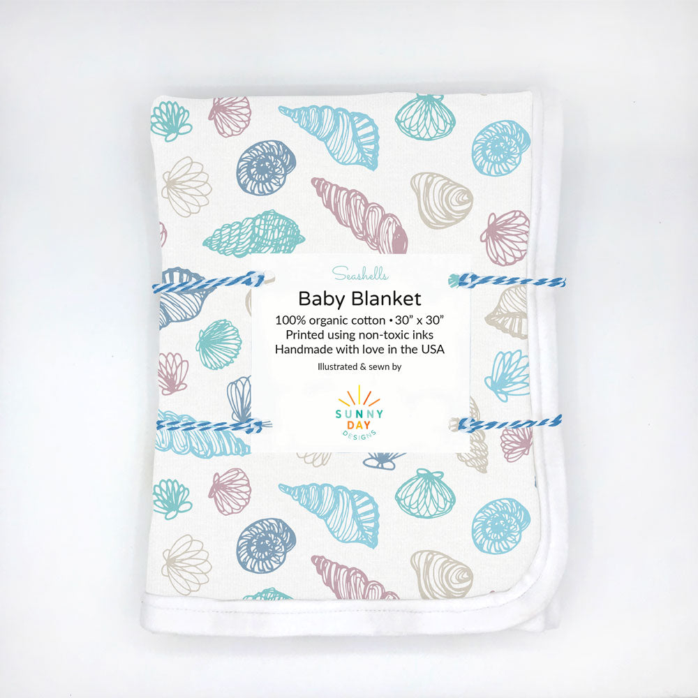 Seashells printed organic cotton baby blanket by Sunny Day Designs is folded and packaged using colorful baker's twine against a white background. Made in the USA, featuring a coastal, nautical shell themed print