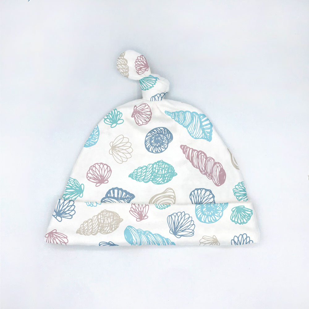 Seashell printed organic cotton baby hat on a white background. Designed and sewn by Sunny Day Designs, featuring turquoise, blue, gray, and dusty purple scribble seashell shapes. made in the USA.