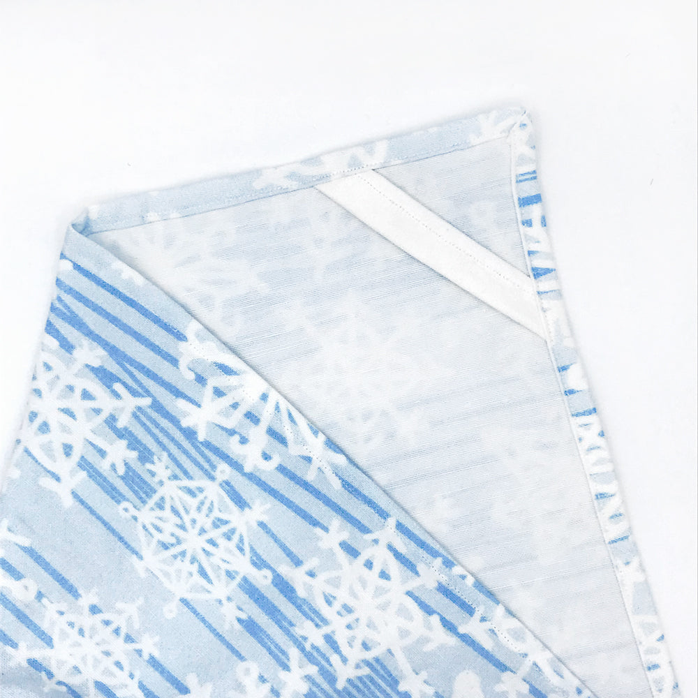 A corner view of a Snowflake printed kitchen tea towel by Sunny Day Designs, which is blue/white and made out of linen/cotton fabric. Made in the USA. Photo shows a corner of tea towel with white corner hanging loop.