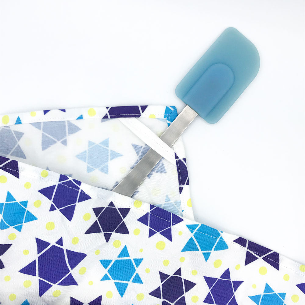 A close up view of our Star Of David printed Jewish tea towel by Sunny Day Designs. This image shows the corner hanging loop with a blue spatula looped through the corner. This Jewish dish towel is handmade in the USA and shown on a white background.