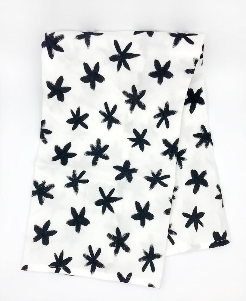 Our black and white abstract star printed dish towel is made in the USA from linen/cotton fabric by Sunny Day Designs. This image shows an unpackaged Starry Eyed tea towel folded in half on a white background.